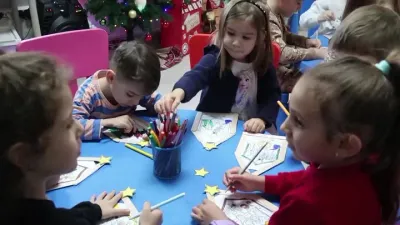 Copii colorând felicitări la masa de lucru, lângă bradul de Crăciun, în atelierul caritabil PlusKids
